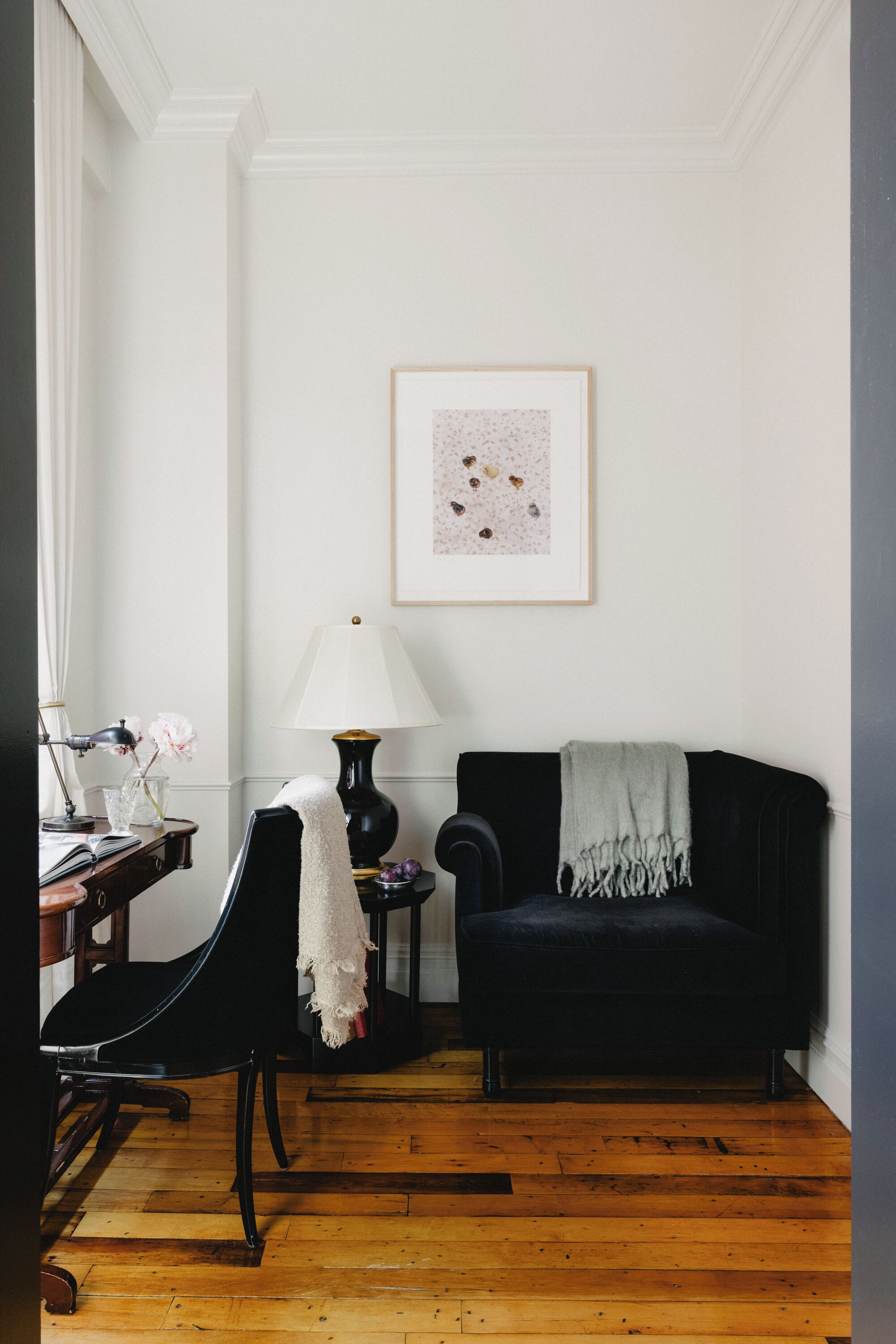 Una habitación con un sofá negro, un escritorio con lámpara y un cuadro en la pared.