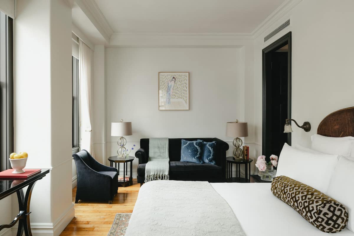 Una camera d'hotel con un letto, un divano, una sedia, un tavolino e un comodino.