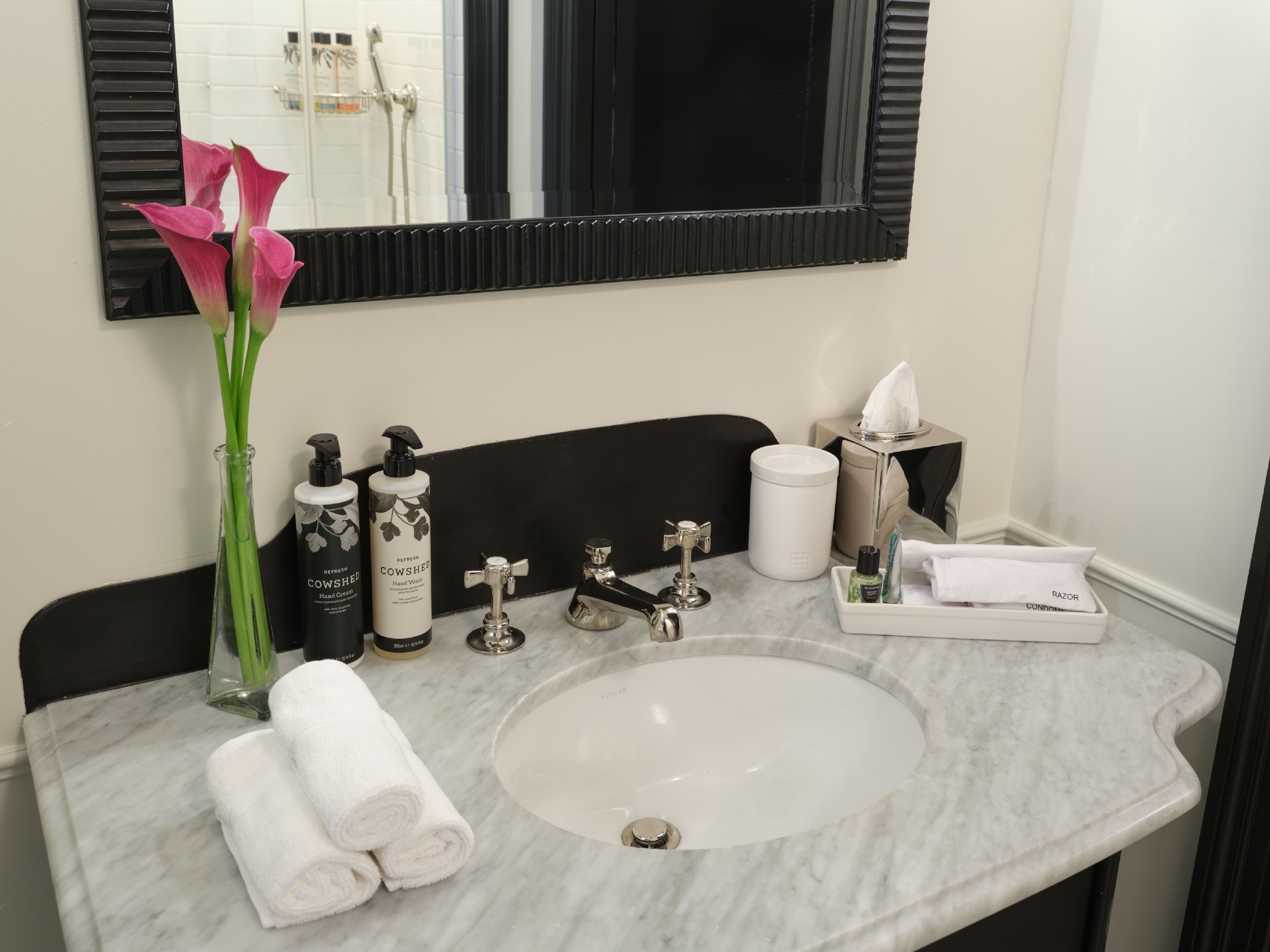 A bathroom with a marble sink, a mirror, a vase with flowers, toiletries, and towels.