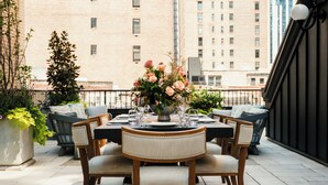 A rooftop terrace with a round table set for dining, surrounded by cushioned chairs. - The Ned NoMad (New York)