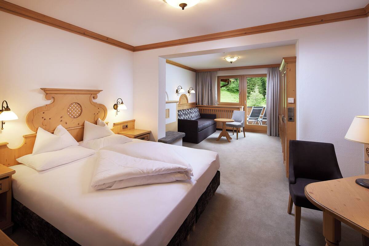 A hotel room with a large bed, a desk, a chair, and a view of the outdoors.