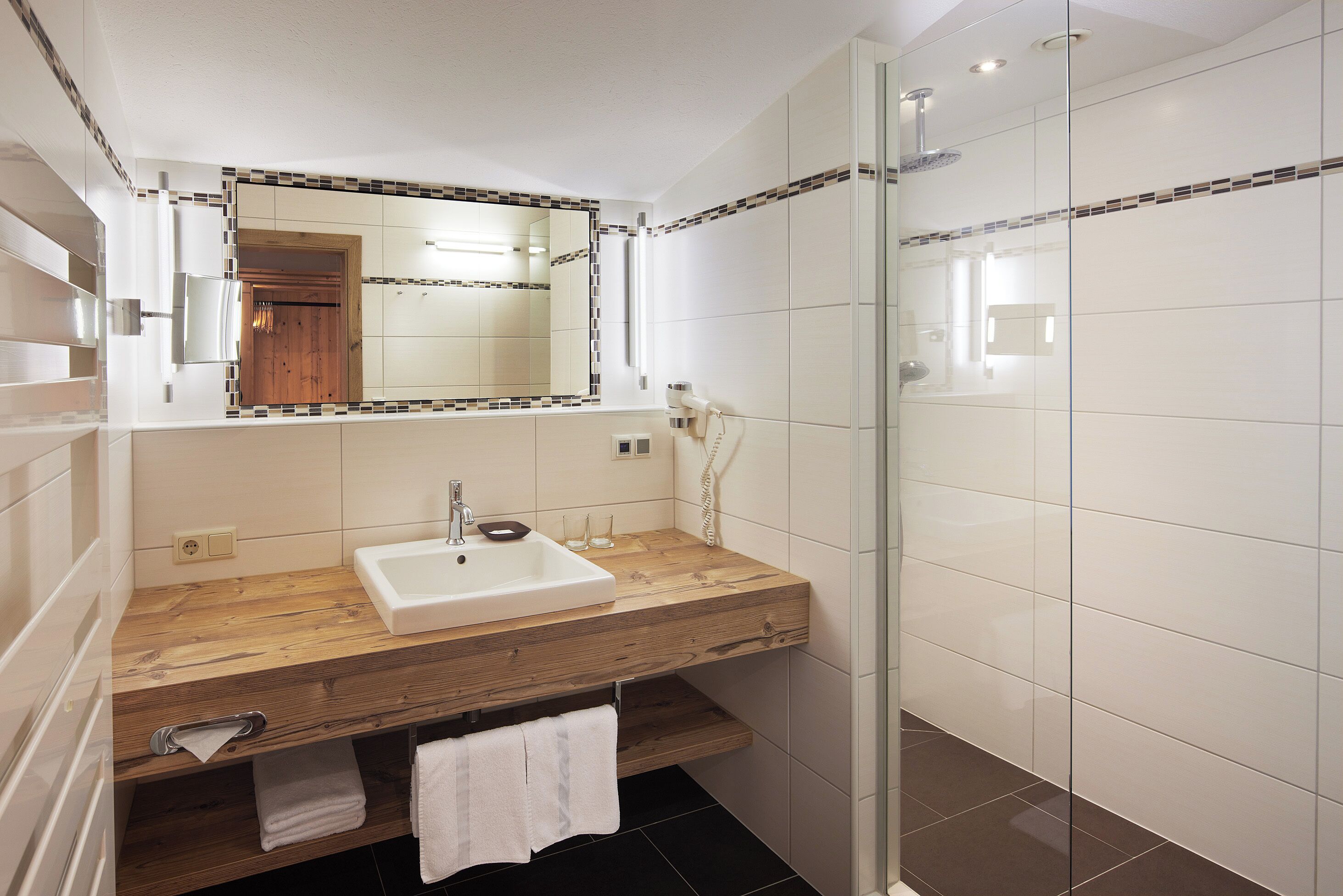 A modern bathroom with a wooden vanity, a large mirror, a glass-enclosed shower, and a white sink.