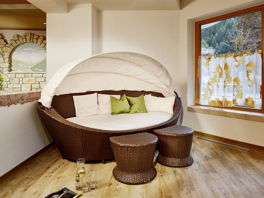 A wicker sofa bed with a canopy, two matching stools, and a glass of water on a wooden floor.