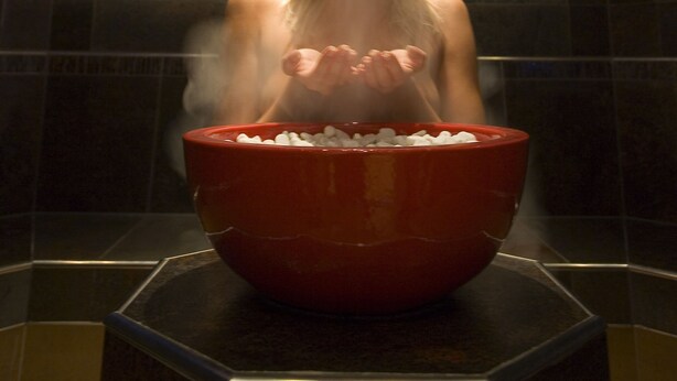 Une personne se trouve dans un hammam, avec un grand bol rouge devant elle.