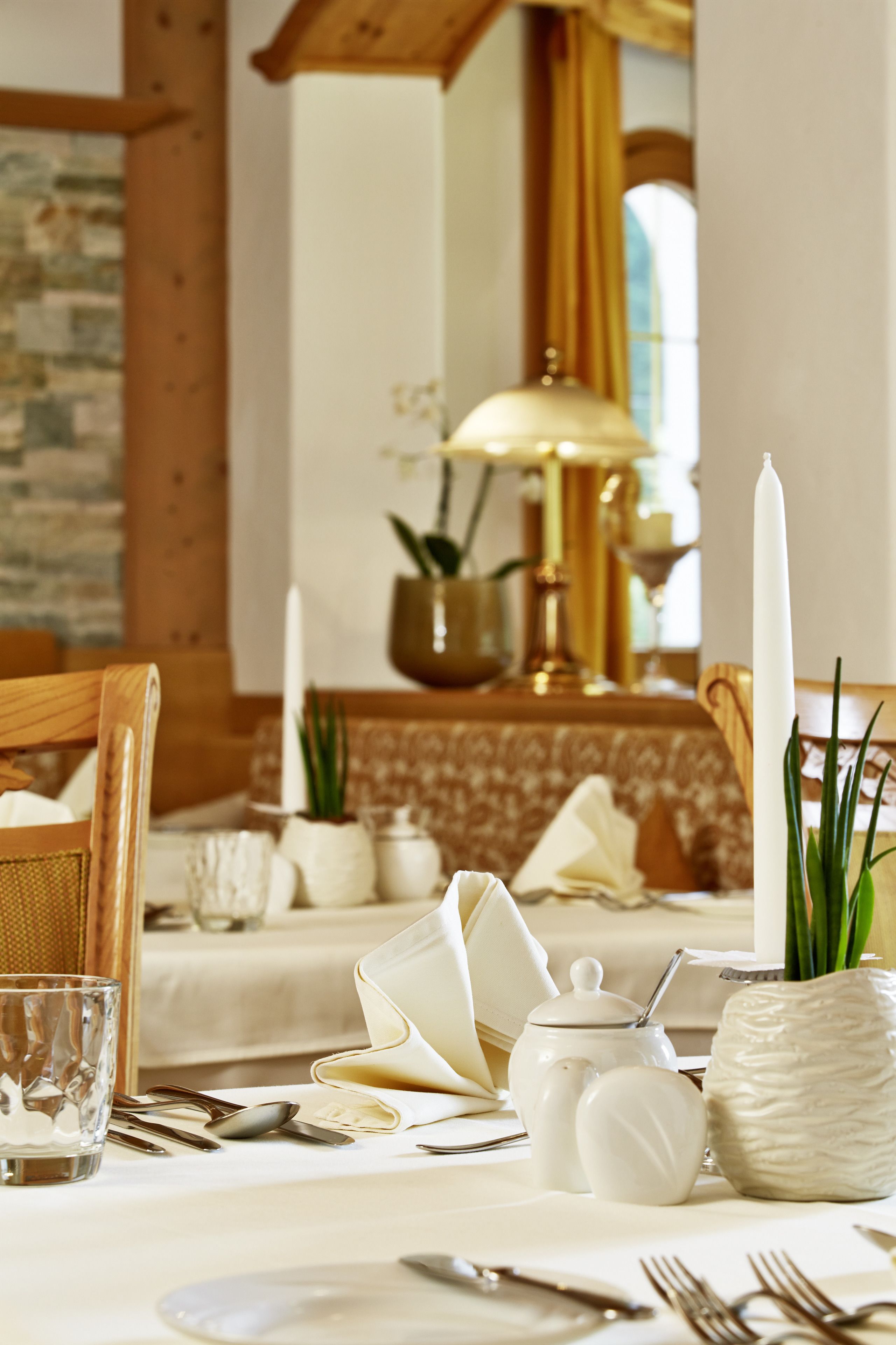 A dining table set with white tableware, a candle, and a vase with green plants.