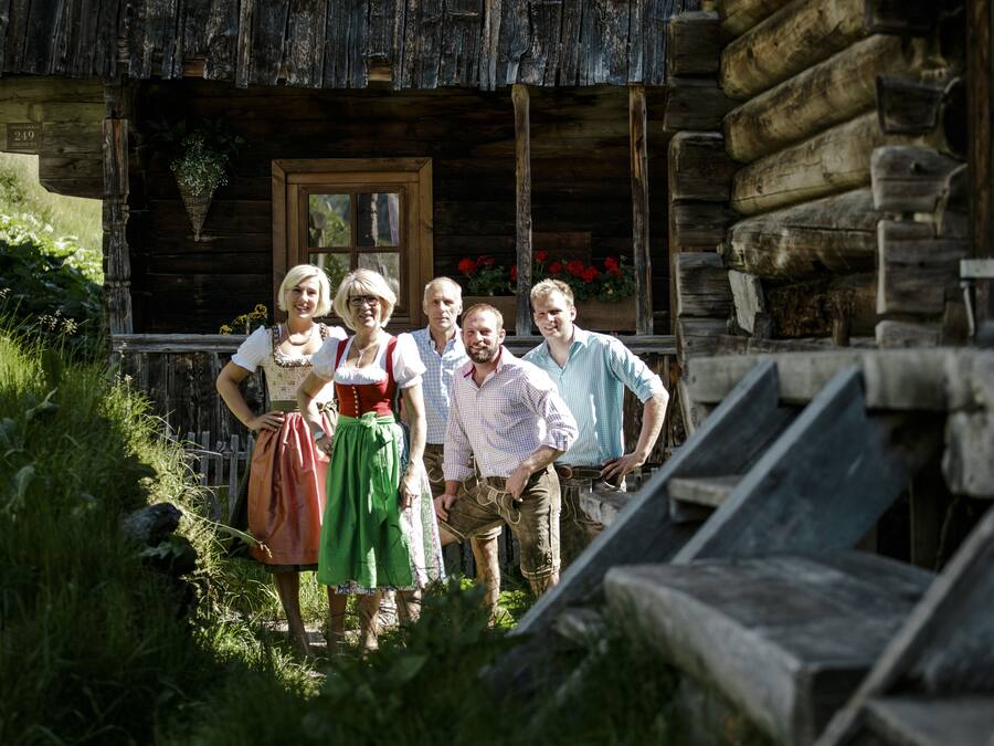 A rustic wooden cabin with a wooden door and a window, surrounded by greenery.