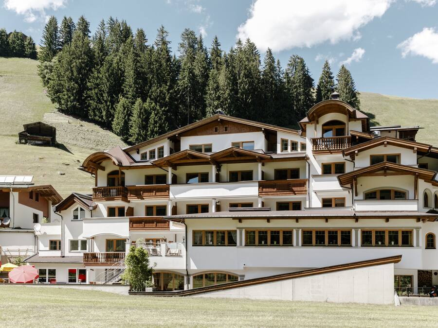 A multi-story hotel with balconies, a ski lift, and a mountainous backdrop.