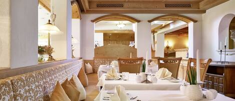 A dining area with tables set for a meal, wooden beams on the ceiling, and a bench along the wall.