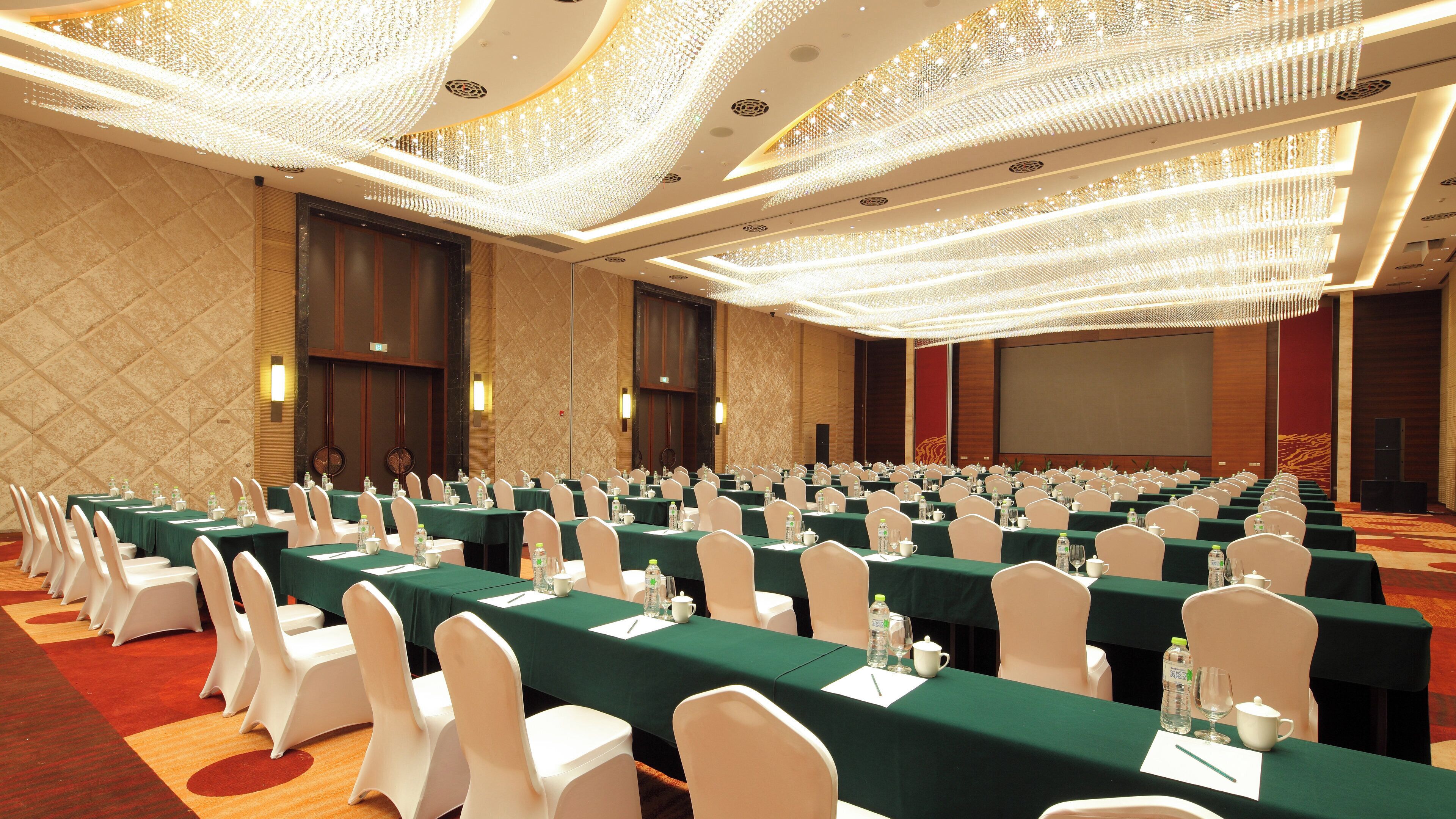 A conference room with rows of tables, chairs, and a large screen.