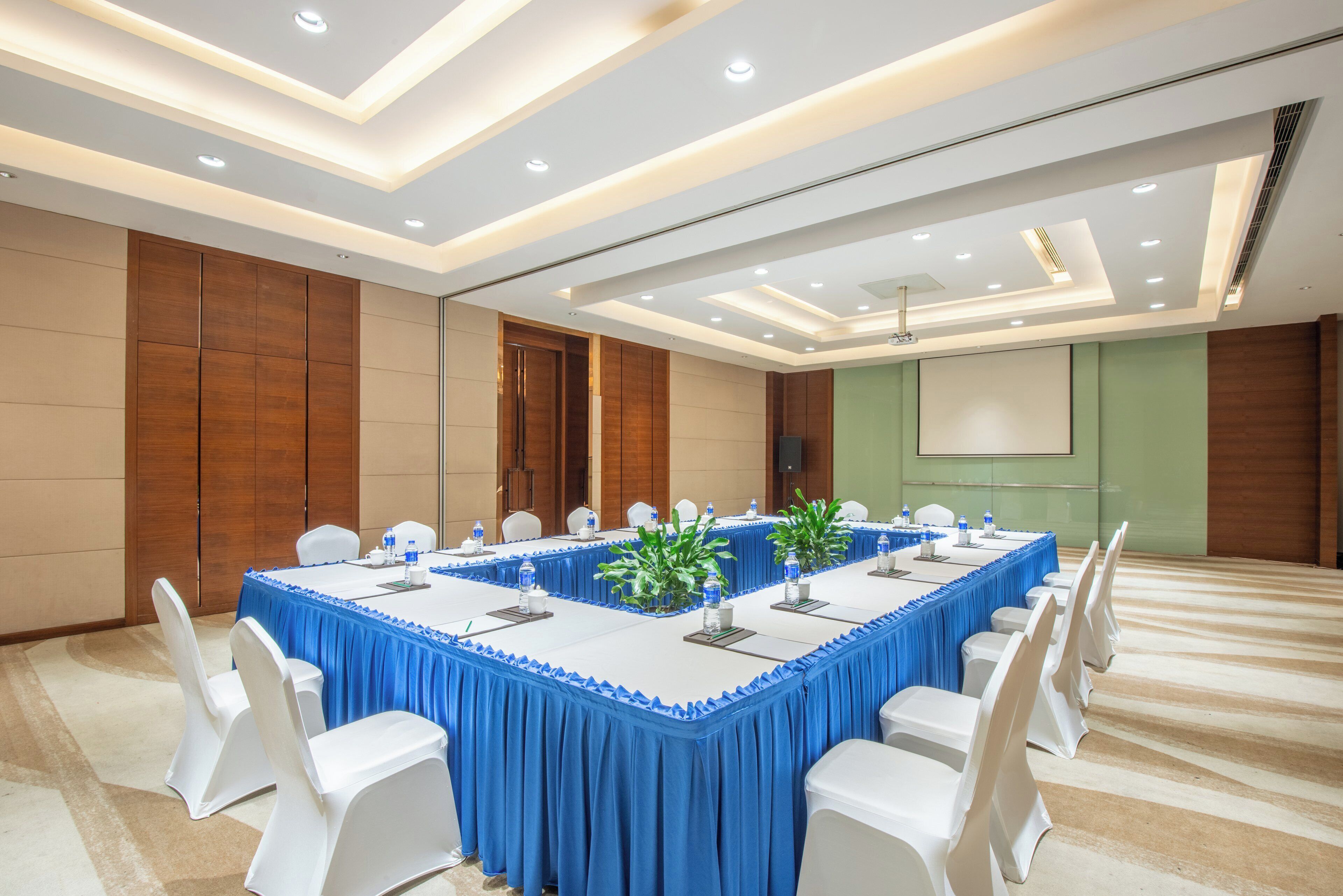 A conference room with a long table, white chairs, and a projector screen.