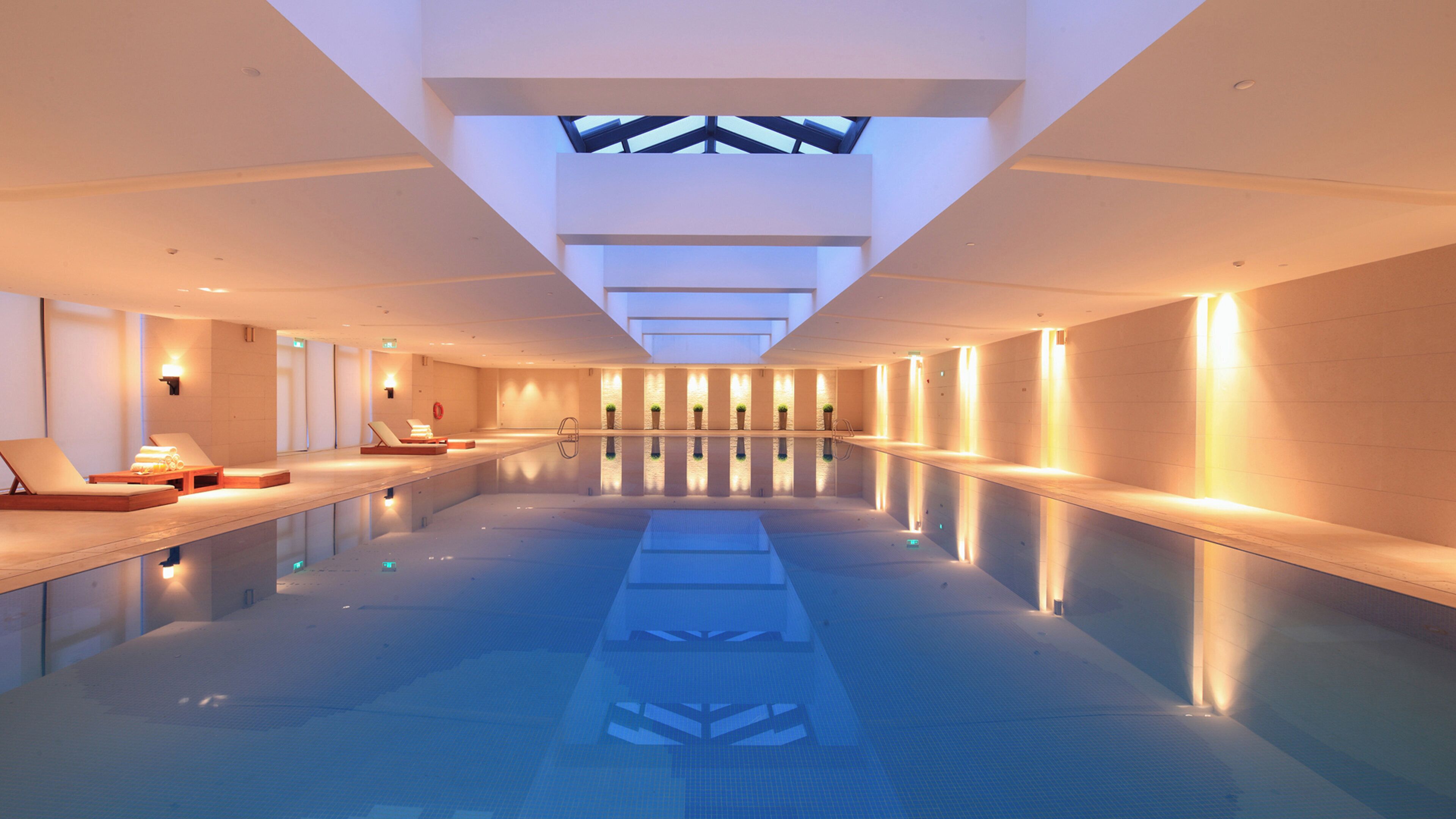 Una amplia piscina interior con tragaluces, sillas de descanso y un diseño moderno y limpio.