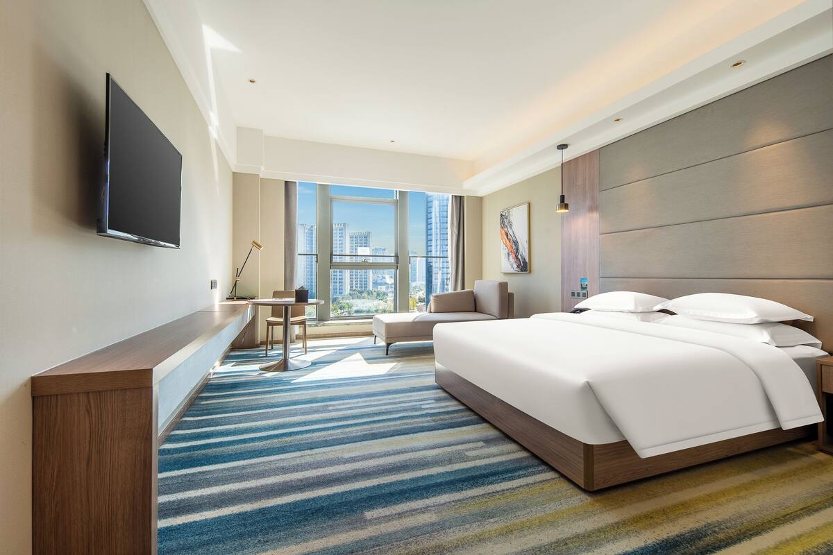 A modern hotel room with a large bed, a desk, and a TV mounted on the wall.