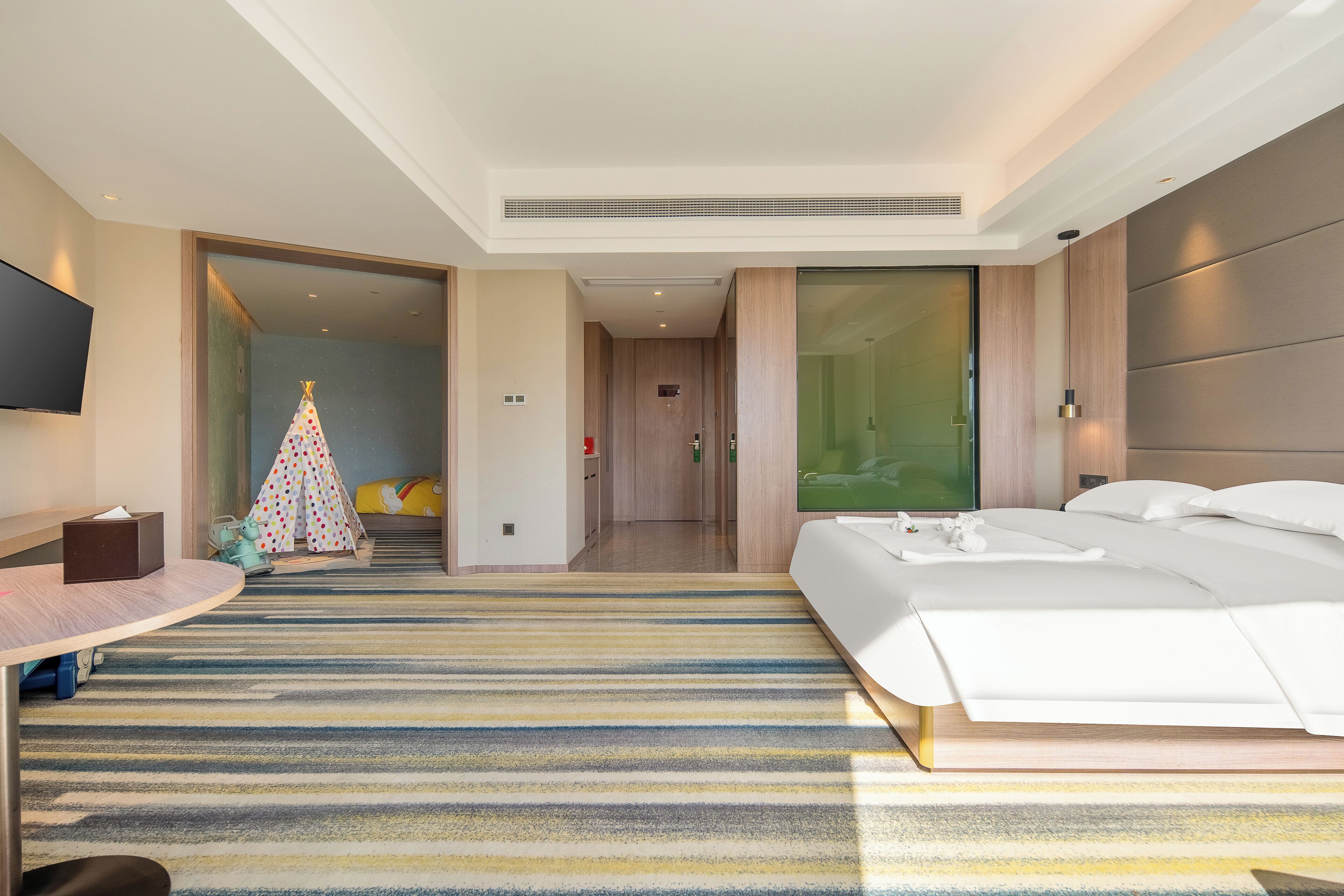 Une chambre d’hôtel moderne avec un grand lit, un bureau, une télévision et une moquette rayée aux couleurs vives.