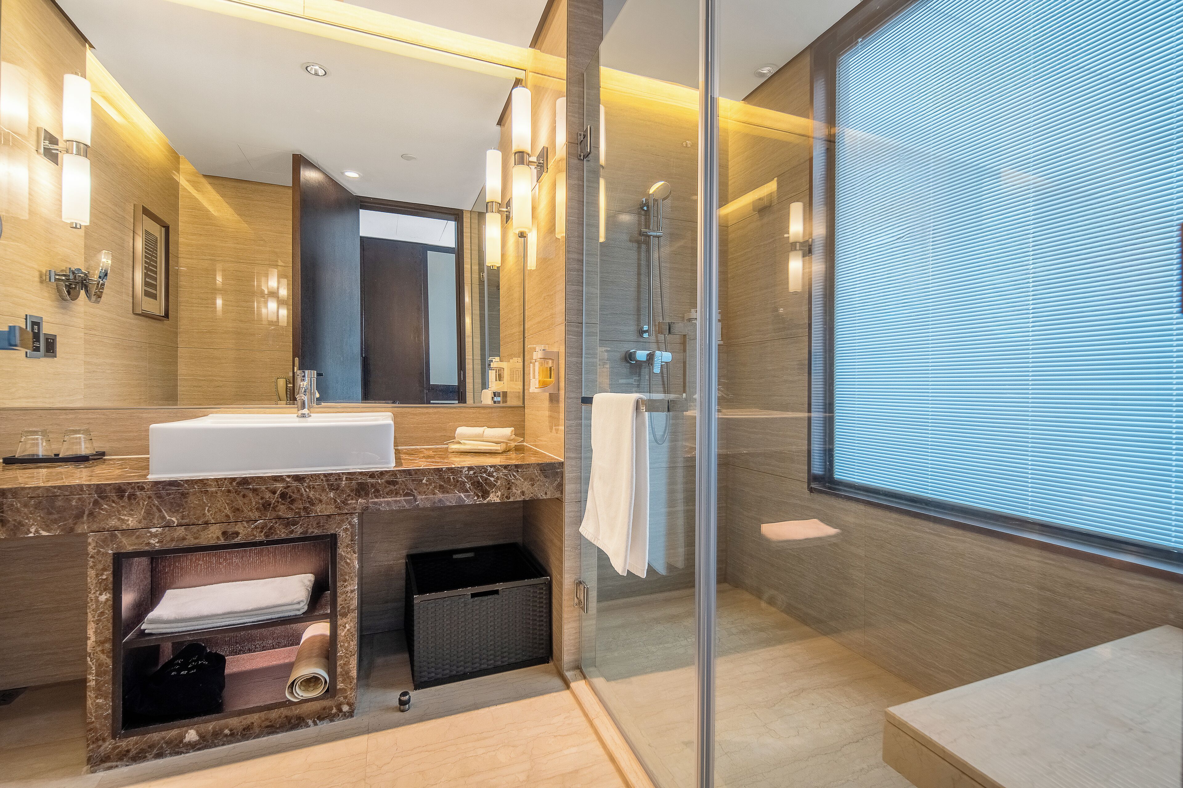 A modern bathroom with a glass-enclosed shower, a large mirror, and a marble countertop.