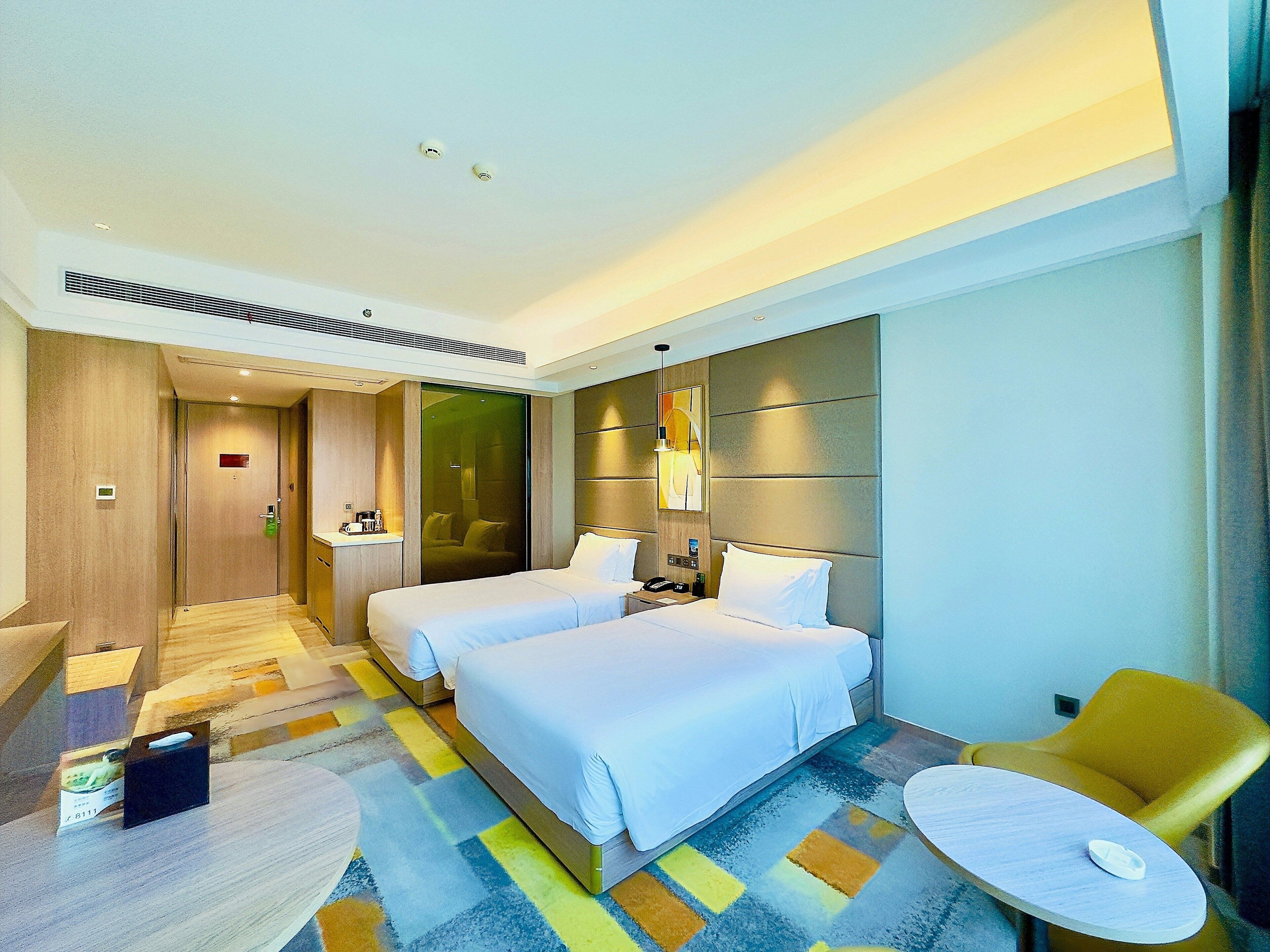 A hotel room with two beds, a desk, a chair, a small table, and a bathroom door.