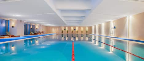 An indoor swimming pool with clear lanes, lounge chairs, and a skylight above.