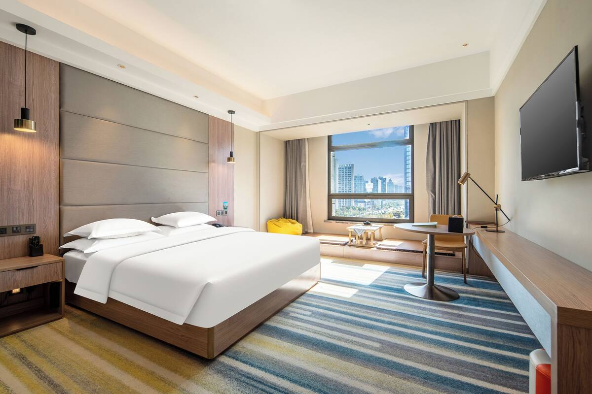 A modern hotel room with a large bed, a desk, a chair, and a TV.