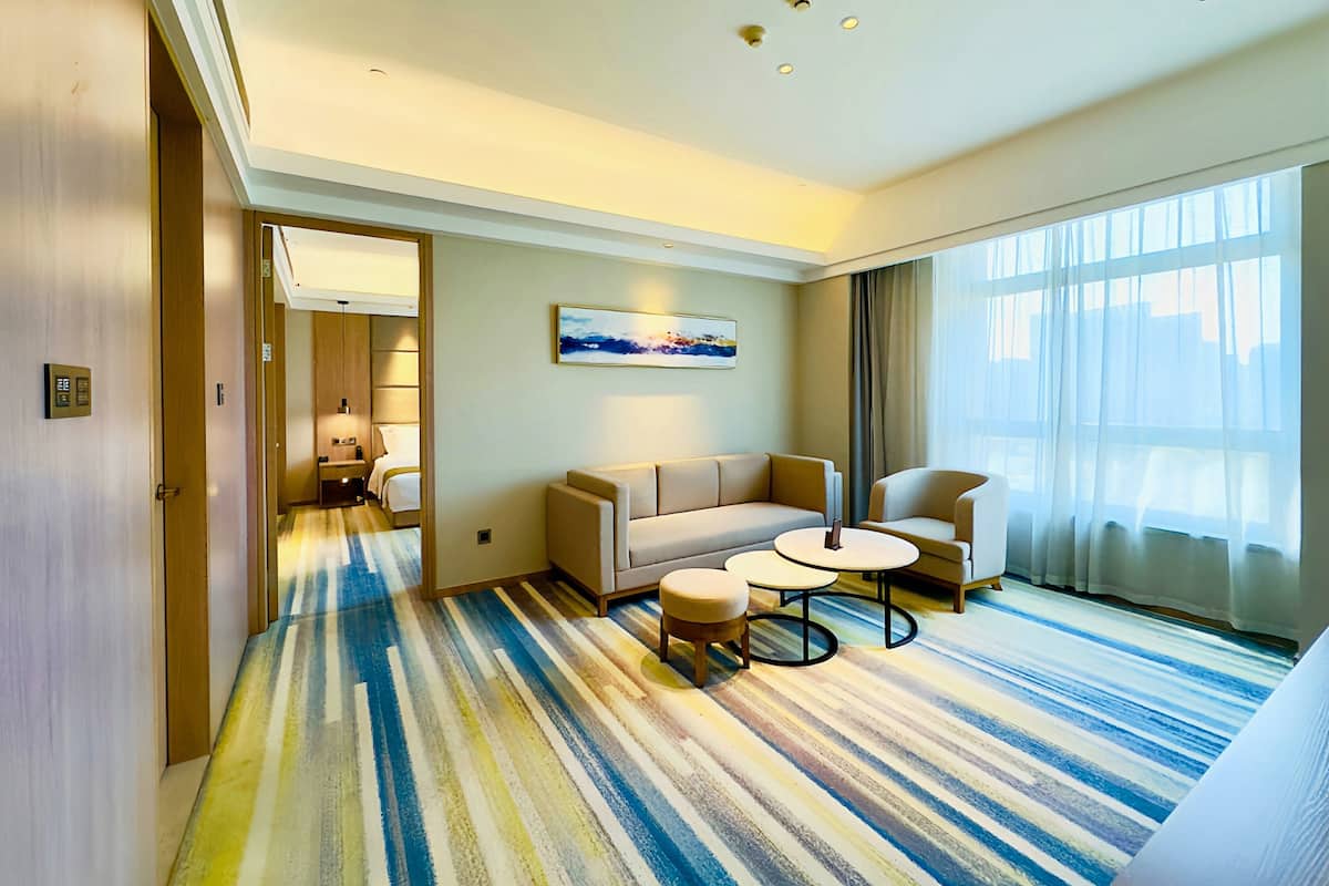 A hotel room with a striped carpet, a sofa, a chair, a small table, and a painting on the wall.