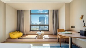 Habitació d'hotel moderna amb una finestra gran, un sofà de sacs groc, una taula petita i una cadira.