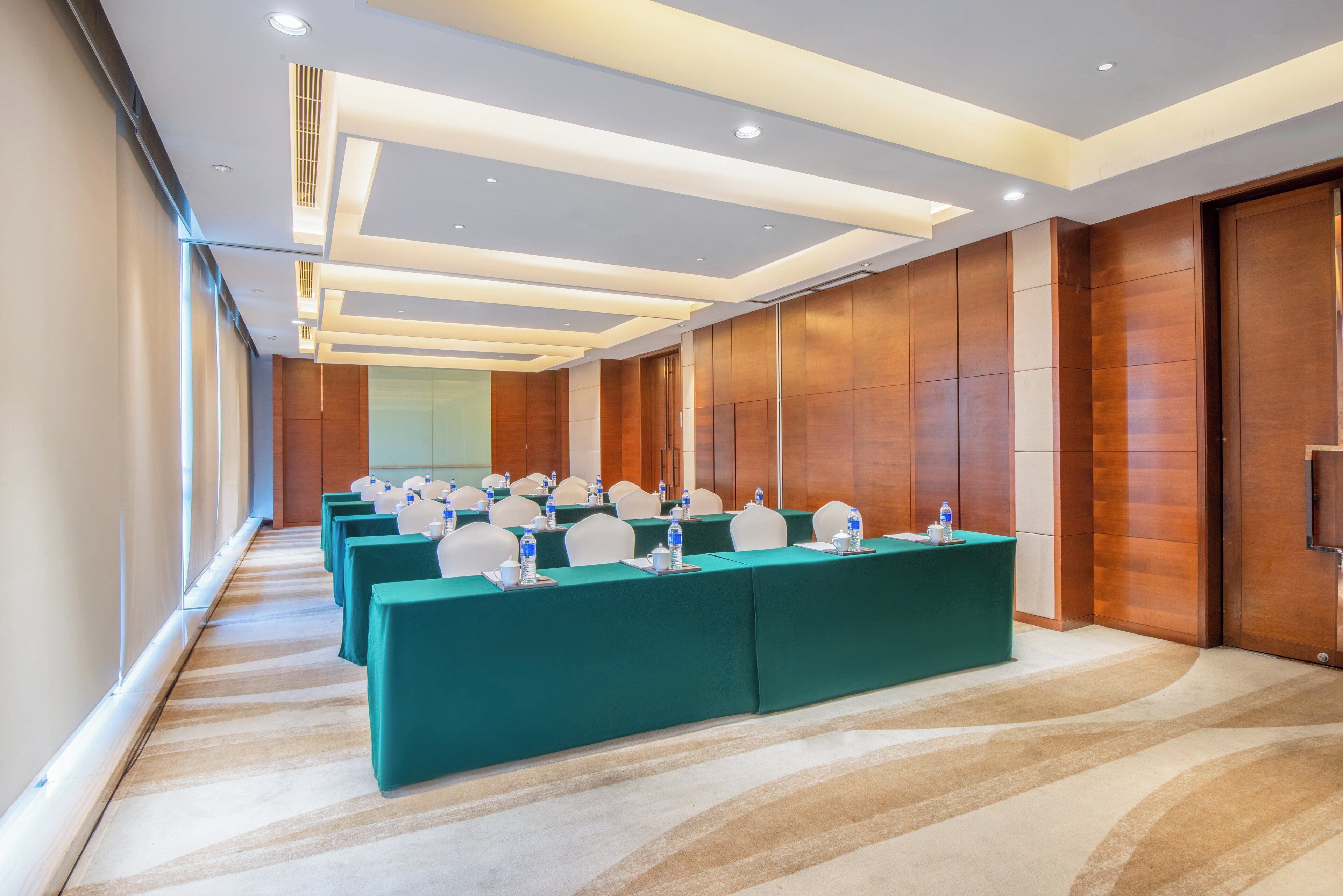 Un salón de conferencias con largas mesas, sillas y botellas de agua.