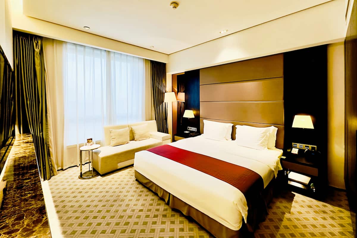 A hotel room with a large bed, a sofa, a small table, and a nightstand.