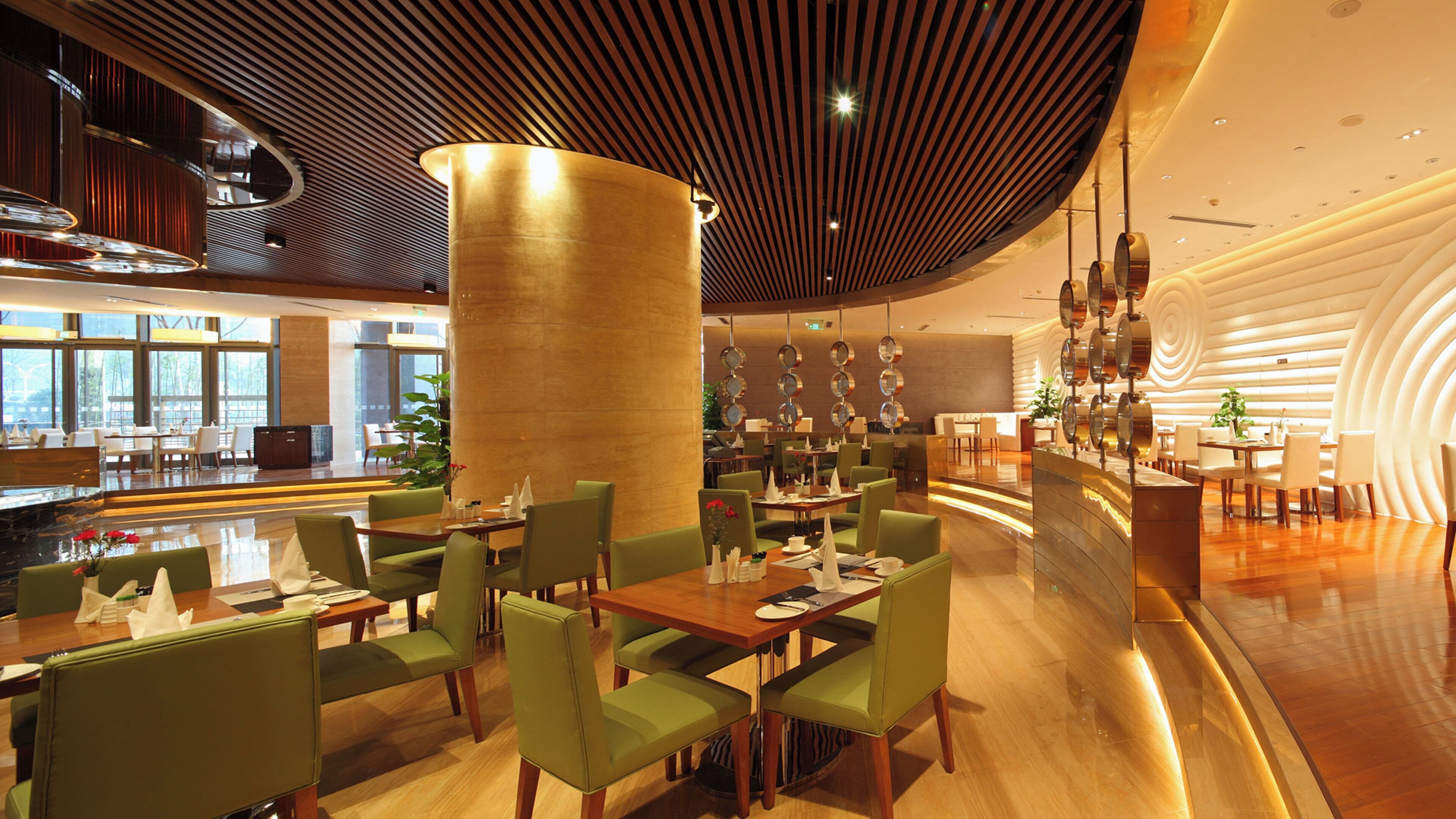 A modern restaurant interior with green upholstered chairs, wooden tables, and a unique ceiling design.