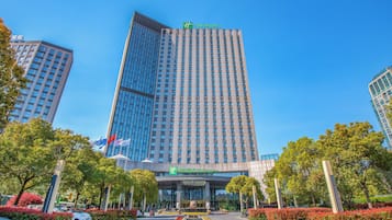 Un hotel de gran altura con fachada de vidrio moderna, un patio central con macizos de flores y un cielo azul despejado.