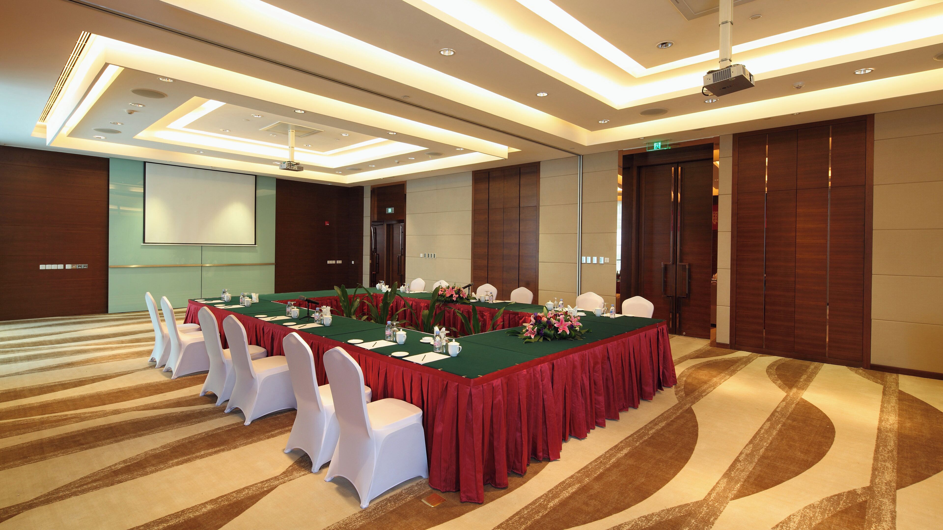 A conference room with a long table, white chairs, and red tablecloths.