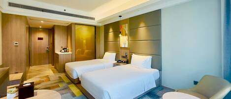 A hotel room with two beds, a desk, a chair, and a small table.