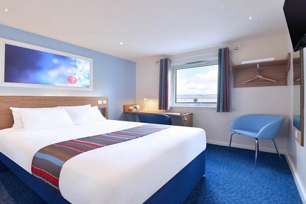 Ein Hotelzimmer mit einem großen Bett, einem Schreibtisch, einem Stuhl, einem Fernseher und einem Fenster mit Vorhängen.
