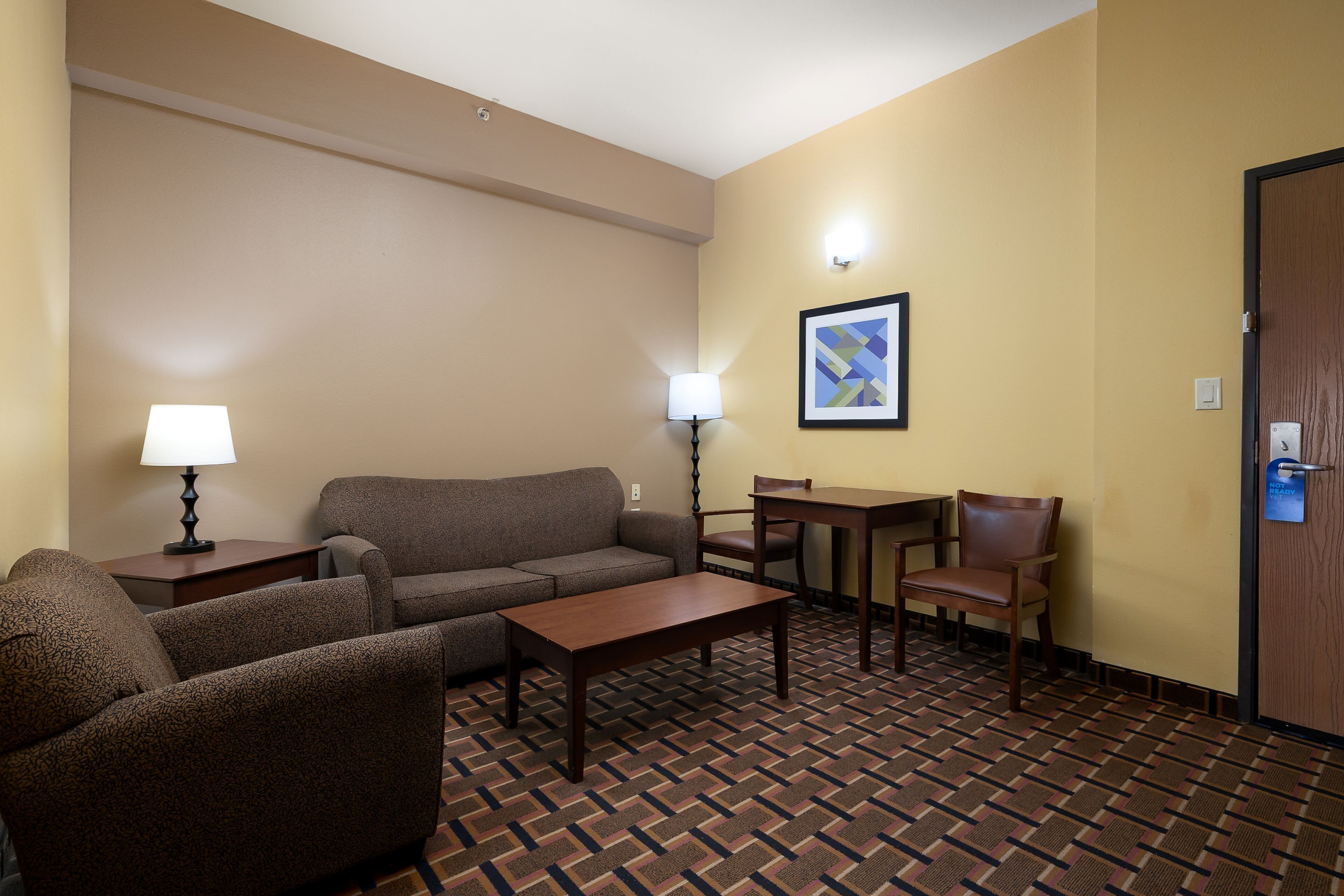 Habitación de hotel con sofá, sillón, mesa, lámpara y un cuadro en la pared.