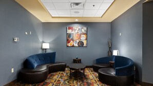 A lounge area with two blue sofas, a small round table, and a colorful patterned carpet. - Holiday Inn Express and Suites George West by IHG (George West)