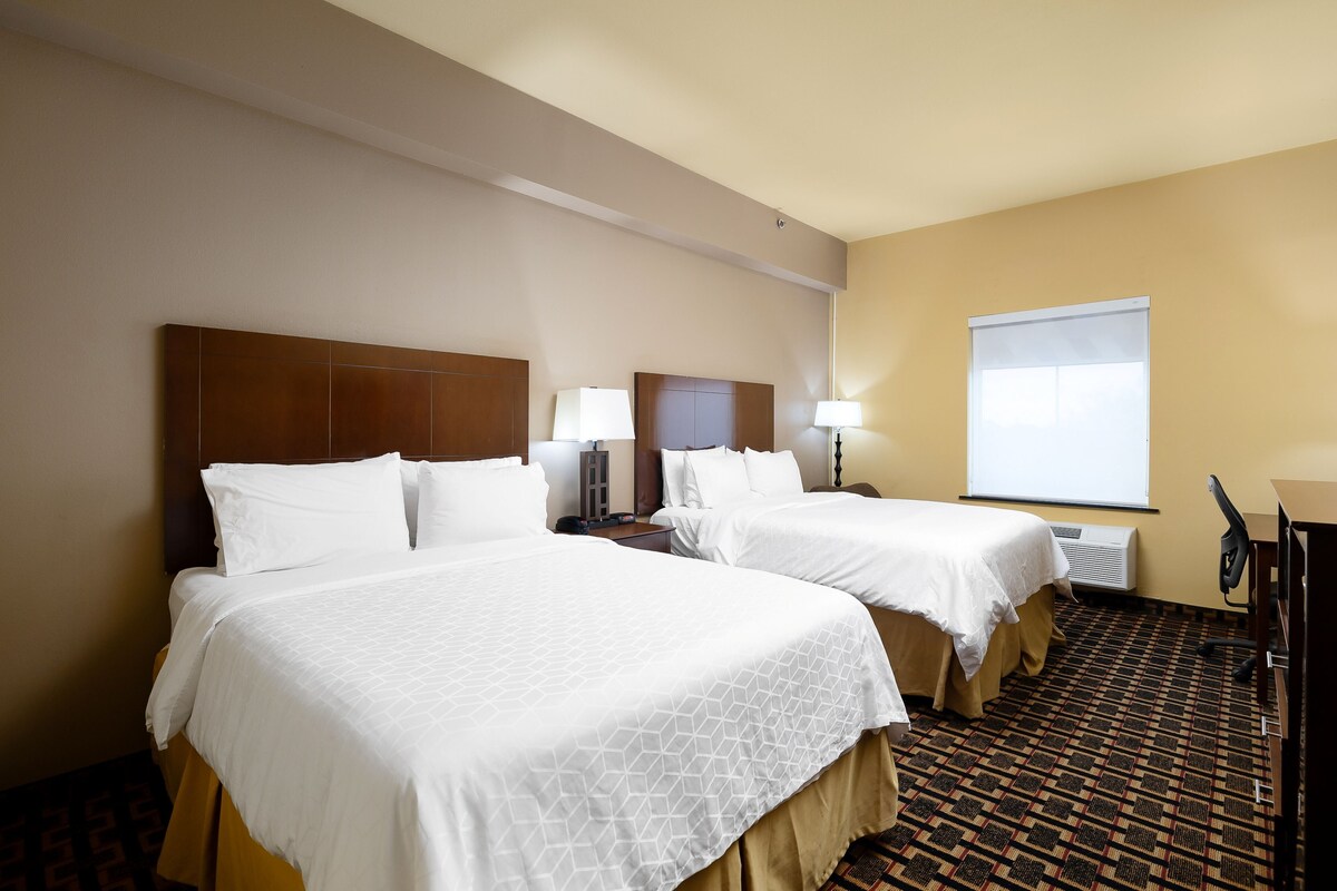 A hotel room with two beds, a desk, and a window with blinds.
