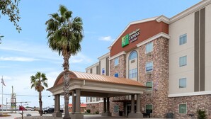 A Holiday Inn Express & Suites building with a stone facade, a covered entrance, and palm trees. - Holiday Inn Express and Suites George West by IHG (George West)