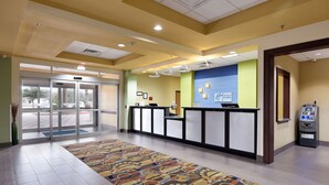 A hotel reception area with a check-in counter, a self-service kiosk, and a patterned carpet. - Holiday Inn Express and Suites George West by IHG (George West)