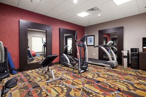 A gym with exercise equipment, mirrors, and a patterned carpet.