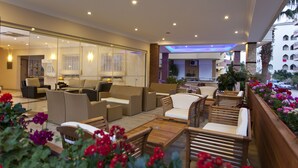 Un vestíbulo de hotel con muebles de mimbre, un mostrador de recepción y vista a la calle.