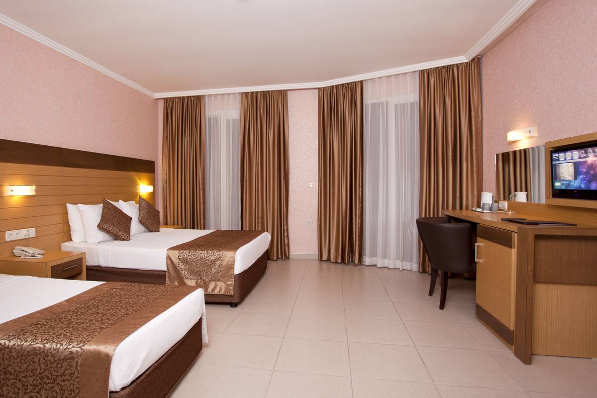 Una habitación de hotel con dos camas, un escritorio, una silla, un televisor y un minibar.