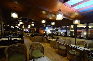 A restaurant with wicker furniture, hanging lights, and a view of the street outside. - Hotel Northfield (Kathmandu)