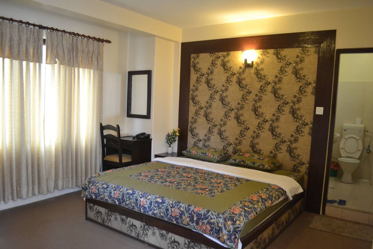 A bedroom with a large bed, a chair, a desk, and a bathroom visible through an open door.