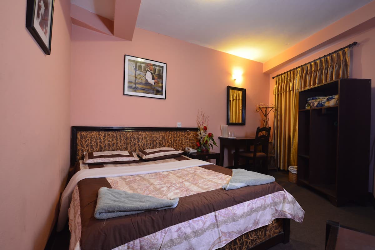 A hotel room with a large bed, a desk, a chair, a wardrobe, and a painting on the wall.