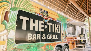 En food truck med tropisk design, med texten âTHE TIKI BAR & GRILLâ pĂ„.