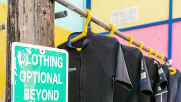 A rack of wetsuits hanging on a wooden post with a sign indicating optional clothing beyond this point.