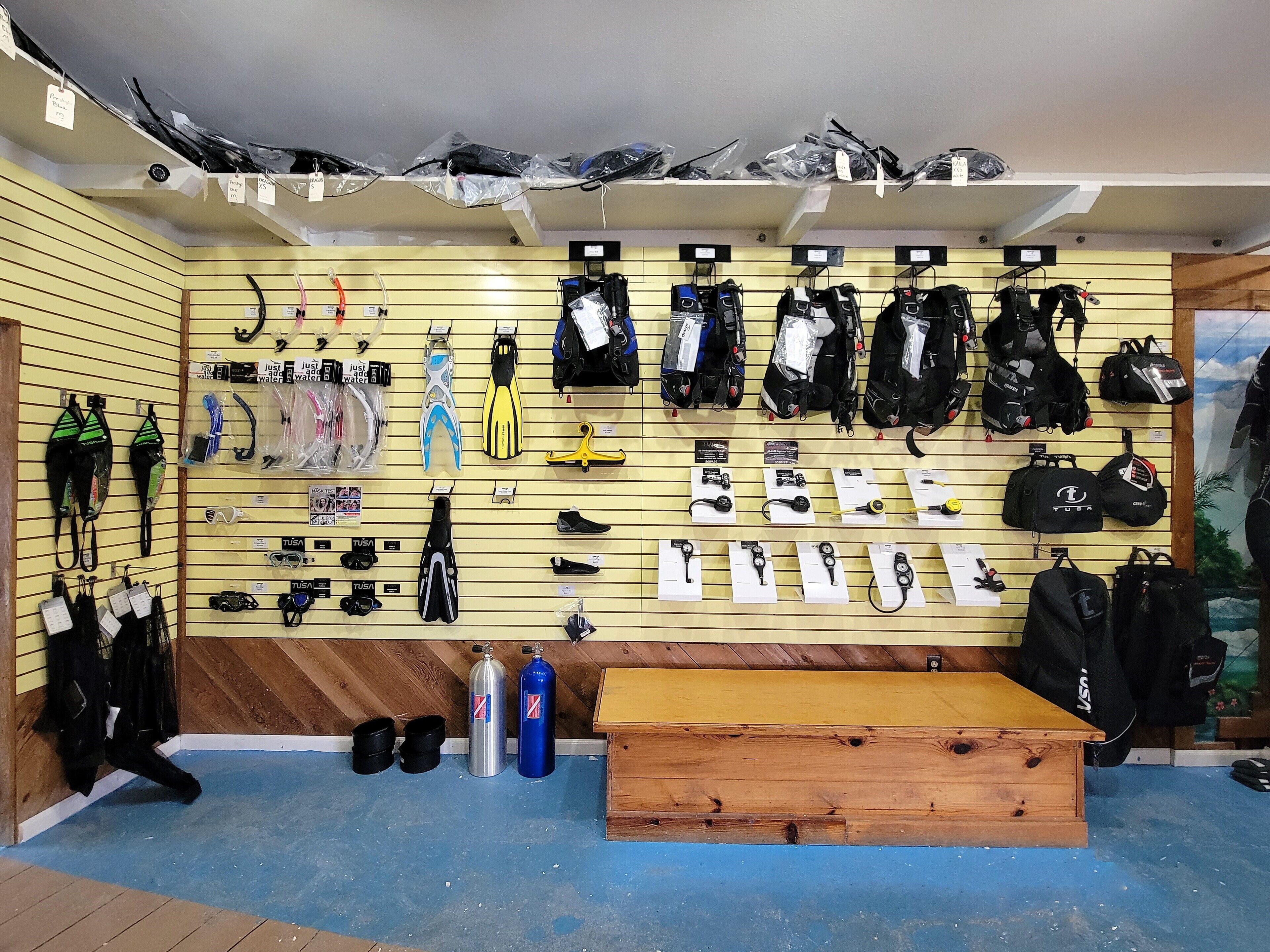 Pared que muestra diverso equipo y accesorios para deportes acuáticos, como trajes de neopreno, aletas y cascos.