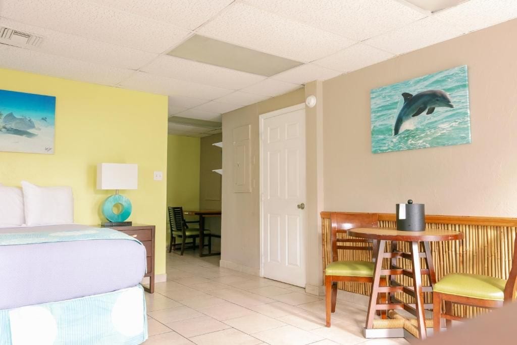 Una habitación de hotel con una cama, una mesa con sillas, un cuadro de delfín y una puerta que da a otra habitación.