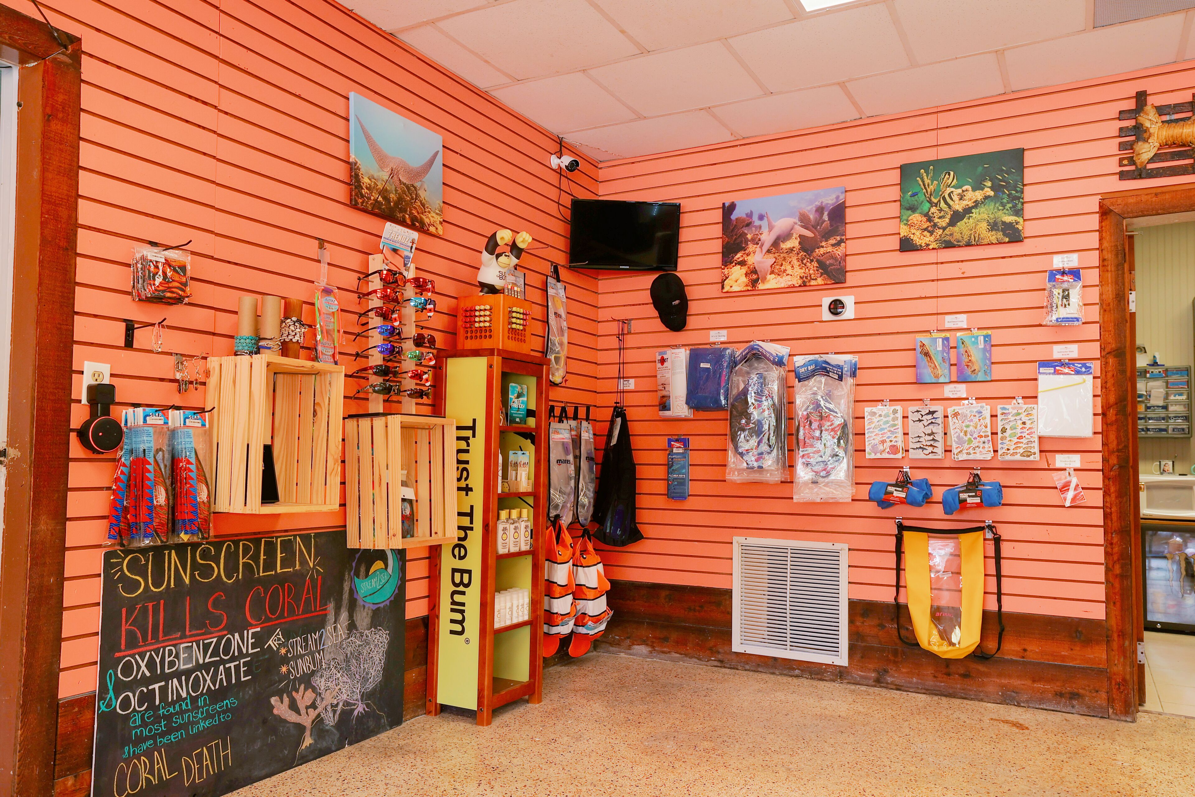 A room with orange walls, a chalkboard with sunscreen information, and various items like bags and sunglasses displayed on shelves.