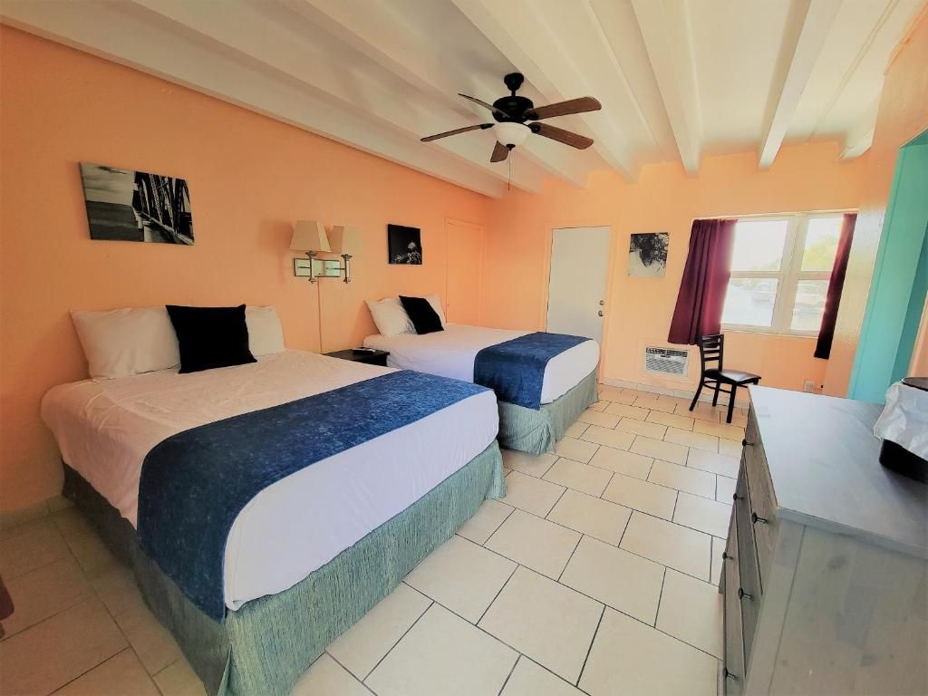 A hotel room with two beds, a ceiling fan, a desk, and a window with curtains.