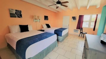A hotel room with two beds, a ceiling fan, a desk, and a window with curtains.