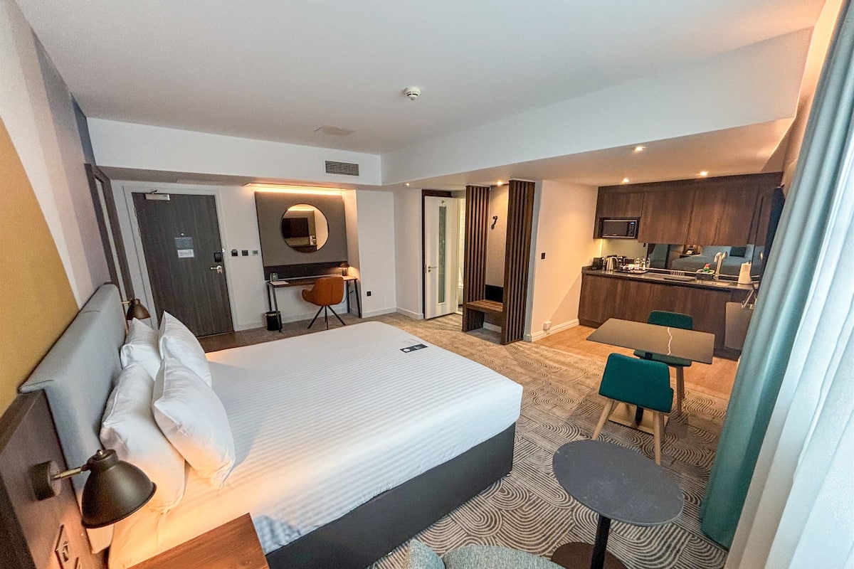 Habitación de hotel con cama, escritorio, silla, kitchenette y baño.