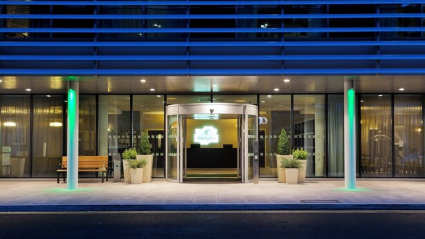 A hotel entrance with a revolving door, glass doors, and potted plants. - Holiday Inn London - Whitechapel by IHG (London)